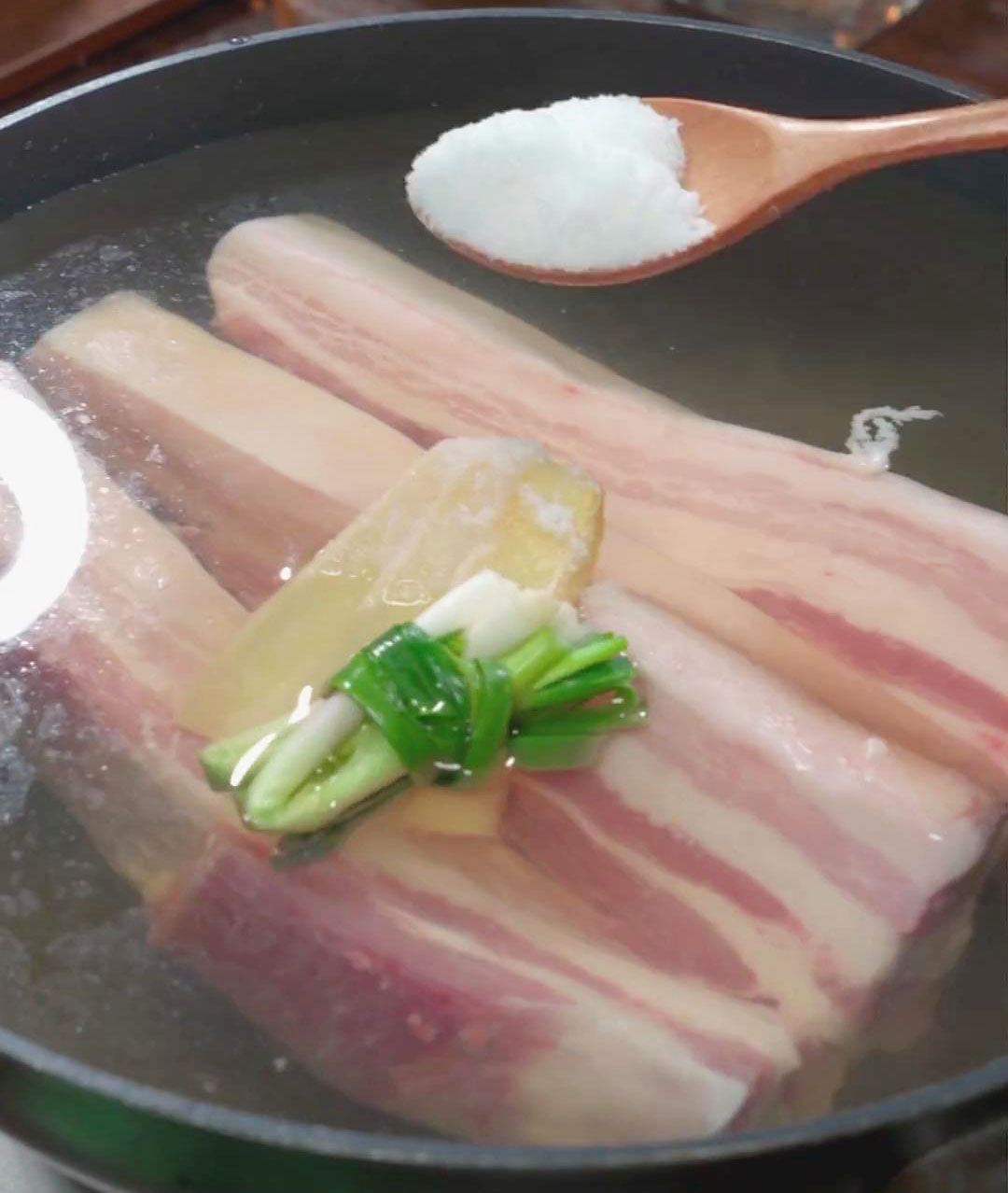 Place the pork belly in the pot along with green onions, ginger slices, cooking wine, and a pinch of salt